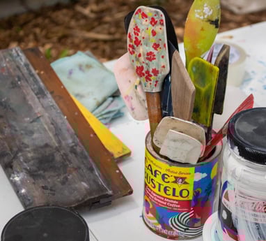 Printmaking materials resting on a table, including spatulas, ink, and a squeegee.