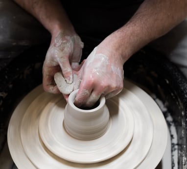 Hands holding a sponge forming a pot on a potter's wheel.