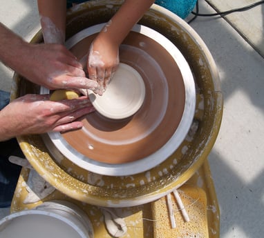 Two hands forming a ceramic bowl on a potter's wheel.