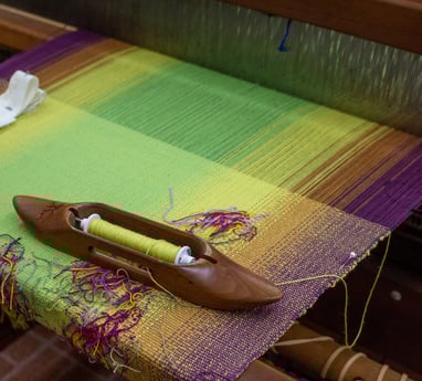 Weaving shuttle resting on an in-progess pieces warped on a loom.