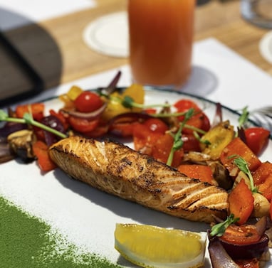 Grilled salmon on a plate surrounded by grilled vegies as an example of healthy meal for someone eating healthy traveling
