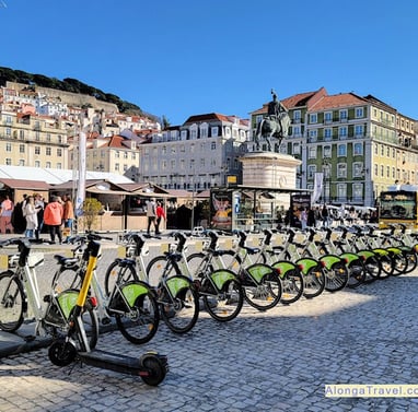 a row of green bikes and bus stops on a busy well planned square in Lisbon