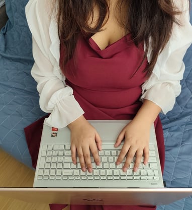 Close-up of a woman’s hands typing on a silver HP laptop, wearing a red dress.