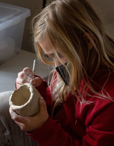 Young girl using a pencil tool to carve into a small ceramic cup.