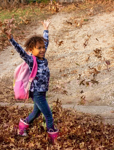 Young girl walking to Access Arts throwing leaves in the air.