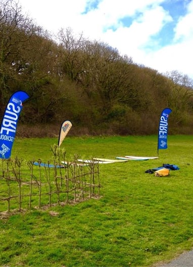 Surfboards laid on grass with surf school teardop flags