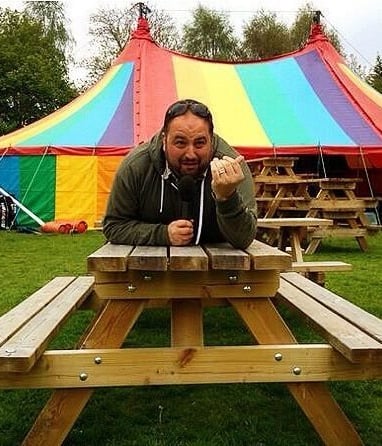 Wynne Evans lying on a picnic beach with a colourful circus tent in the background