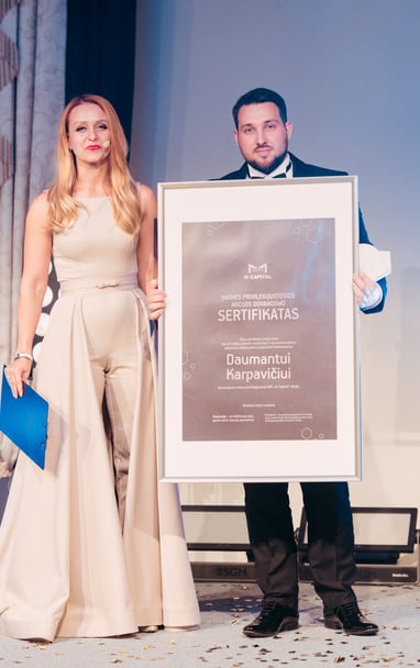 Vyras laiko diplomą šalia stovi moteris su suknele