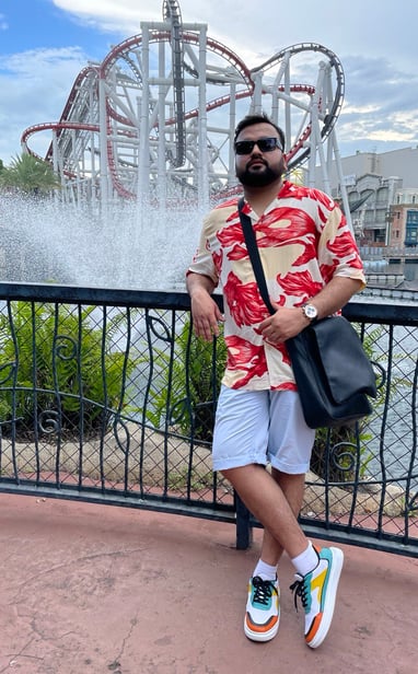 a man in a red shirt and white shorts in front of a roller coaster