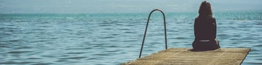 Woman sitting by a lake and looking at the water. How to deal with sadness? Mindletic Blog
