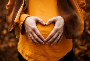 mum to be making a heart shape on her tummy wearing a orange top