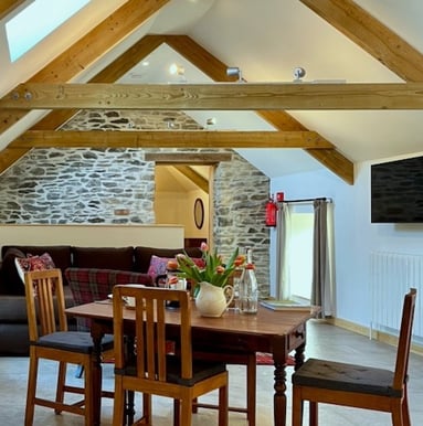 A table and chairs in a room with timber beams and a stone wall