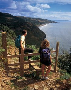 two walkers standing on a hill with a view of the ocean