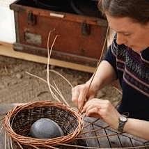 a woman is sitting on a bench weaving a basket