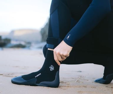 A man pulling on a wetsuit boot at the beach