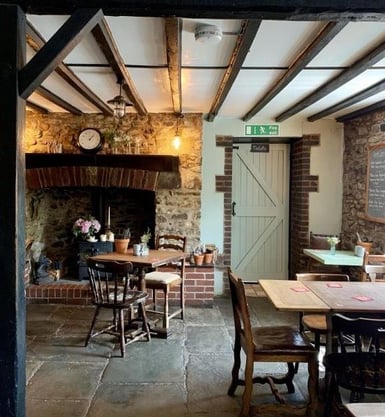 a table and chairs near to a wood burning fire with a clock above it