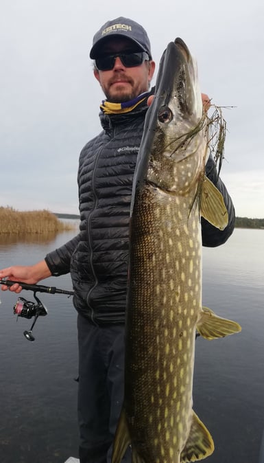 En man har precis fångat en stor gädda i Sverige tack vare Fishing Escape Sweden, han är på en båt.