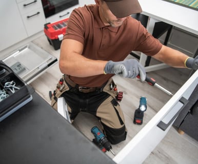 a Handyman in a brown shirt and a tool belt fixing door in New West