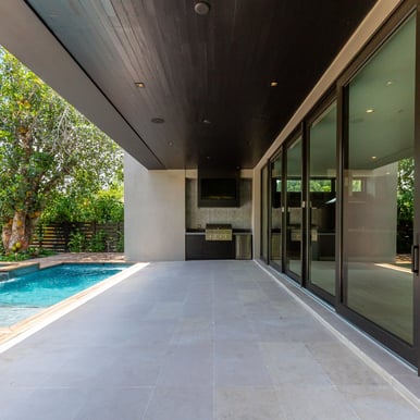 the outside patio of a luxury home with an outdoor grill, pool and deck with sliding glass doors