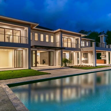 the backyard of a large luxury home showing the back patio and pool at night lit up