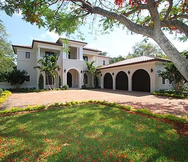 spanish style luxury home with an L shaped driveway and trees and red flowers and autumn leaves