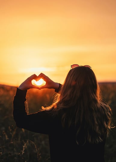 Femme formant un coeur avec ces mains devant un soleil pour etre accompagnée a plonger au coeur