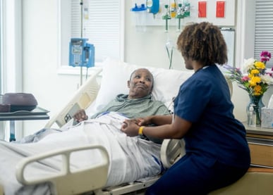 A nurse converses with an elderly man resting in a hospital bed, providing care and support during h