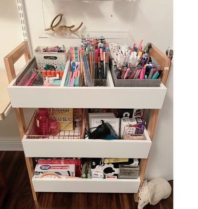 Organized art supply cart with labeled bins, pencils, markers, and craft materials.