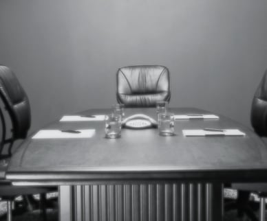 grayscale image of an empty conference room, one chair at the head of the table