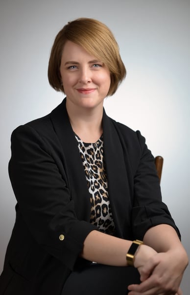 a woman in a black jacket and leopard print top sitting in front of a white background