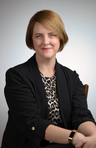 a woman in a black jacket and leopard print top sitting in front of a white background