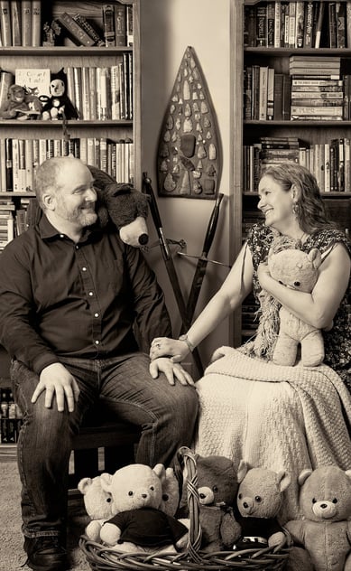 a man and a woman sitting on a chair holding a teddy bear in a library room