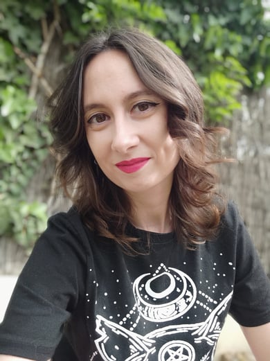 Foto de Reah, la creadora de ADOM. Una mujer castaña vestida de negro sobre un fondo verde de jardín