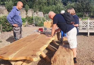 a people standing in front of a wooden bench with a bench and table