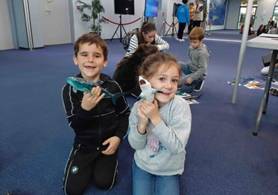 2 enfants avec des maquettes requins dans la main qui sourient