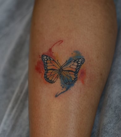 Butterfly tattoo with red and blue watercolor fill on leg by Dudo’s Hyderabad