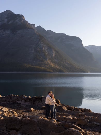 a man and woman standing on rocks in front of a mountain