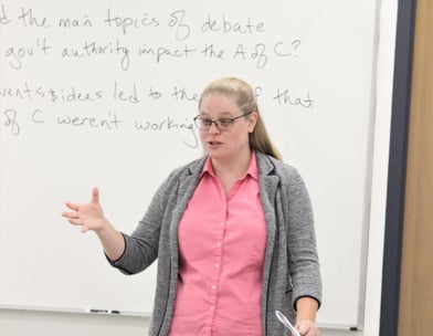 Dr. Hooton in front of a white board at the front of a classroom, teaching.