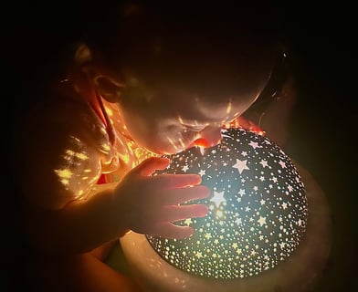 Baby gazing into a blue starry night light, with yellow stars casting on her, as if peering at a new world.