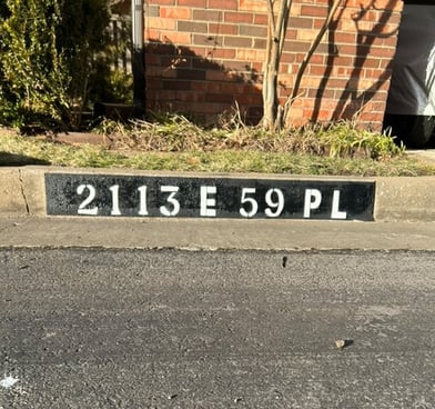 Address "2113 E 59 Pl" painted in black and white on curb.