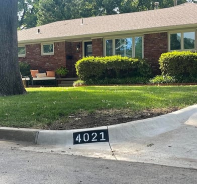 Brick house with a tan roof, shrubs, tree, and curb displaying house number '4021' in white on black