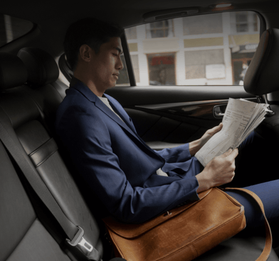 a man in a suit is sitting in a car reading a newspaper