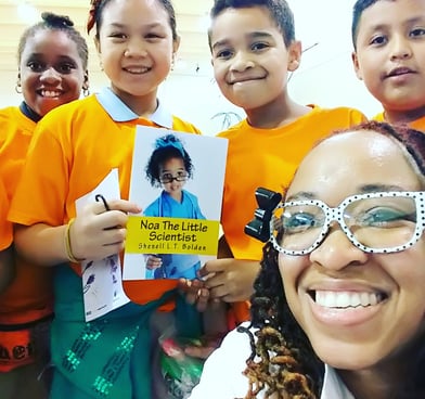 Shenell is in a lab coat smiling with a group of young scholars holding a copy of her book 