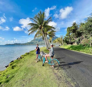 Eva and Manon cycling on a palm-lined road in Bora Bora, French Polynesia.
