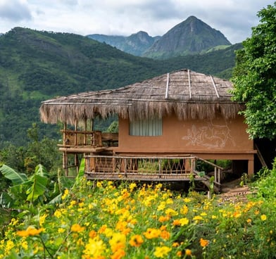 Mud house stay in Kerala with mountains in background.