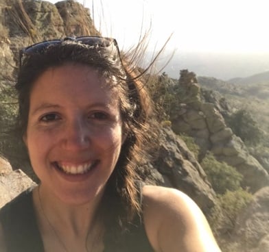 Image description: Sarah Ruth Bates smiles in front of a rocky desert landscape.