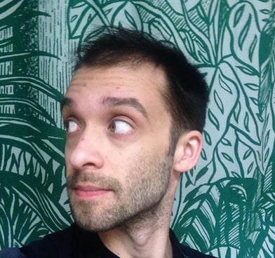 Evan Fleischer looks to the side, standing in front of green patterned wallpaper.