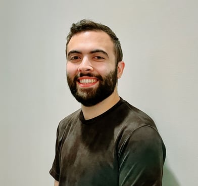 Tarik Dobbs smiles, standing in front of a white wall and wearing a black T-shirt.