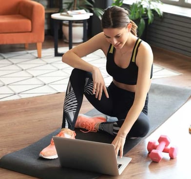 Mulher sorridente com roupa de ginástica fazendo exercícios em casa com tapete de yoga e halteres