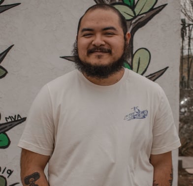 Antonio Villaseñor-Baca smiles at the camera, wearing a white T-shirt and standing against a mural.